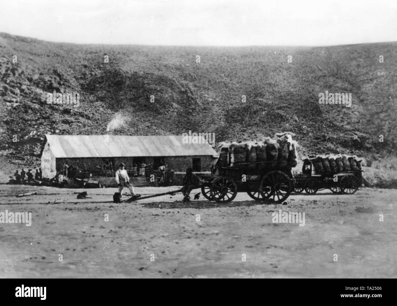 One of the first farm houses in German South West Africa in front of a hill. In the foreground are two heavily loaded wooden carts. (undated photo) Stock Photo