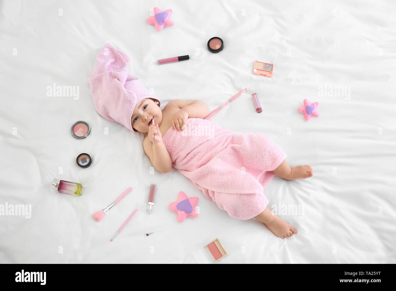 Cute baby girl with cosmetics lying on bed Stock Photo - Alamy