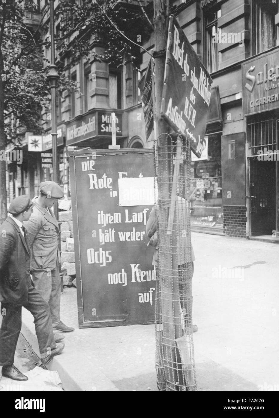 Three men look at a sign of the KPD with the slogan: 'Die Rote Front in ihrem Lauf hält weder Ochs noch Keudel auf'. Stock Photo