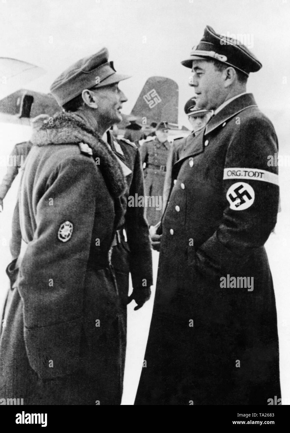 Eduard Dietl and Albert Speer talk at a field airport at the polar circle in Rovaniemi. Albert Speer is Reich Minister for Armament and Ammunition and at the same time is responsible for the organization Todt, whose armband he wears in the picture. Dietl wears a sign of the Gebirgsjaeger (mountain infantry) on his arm. In the background a Focke-Wulf Fw 200. Stock Photo