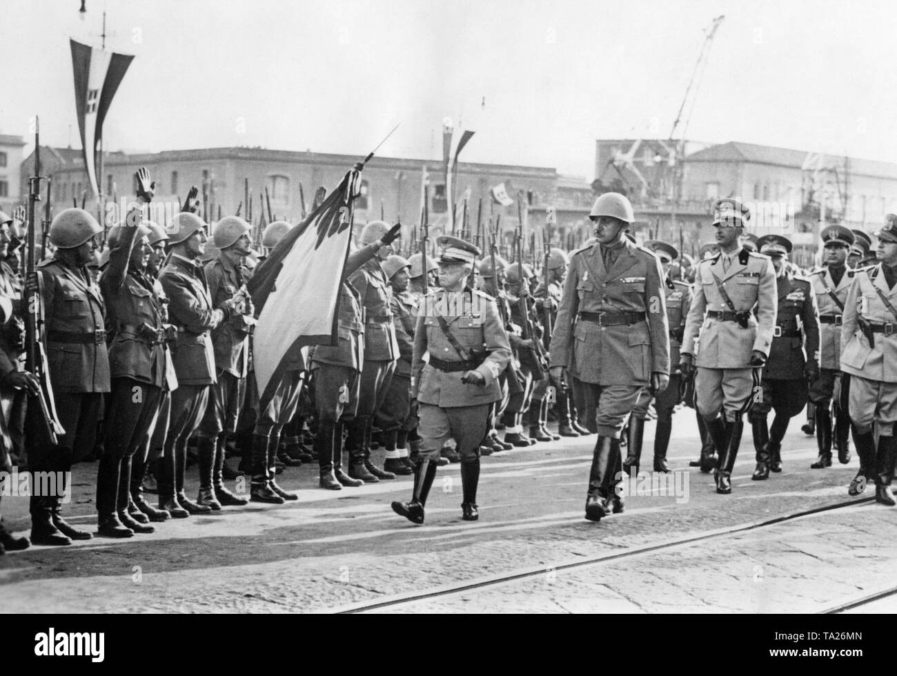 10,000 Italian soldiers, who fought as volunteers on the side of the Franco troops in the Spanish Civil War, are received in the Port of Naples on October 21, 1938. From left to right: King Victor Emmanuel III of Italy, commander of the Legion of General Mario Berti (with steel helmet), Crown Prince Umberto of Savoy (1946, as Umberto II last king of Italy), Gian Galeazzo Ciano (Mussolini's father-in-law, Foreign Minister). On the left, soldiers salute the reception committee with a standard. Stock Photo