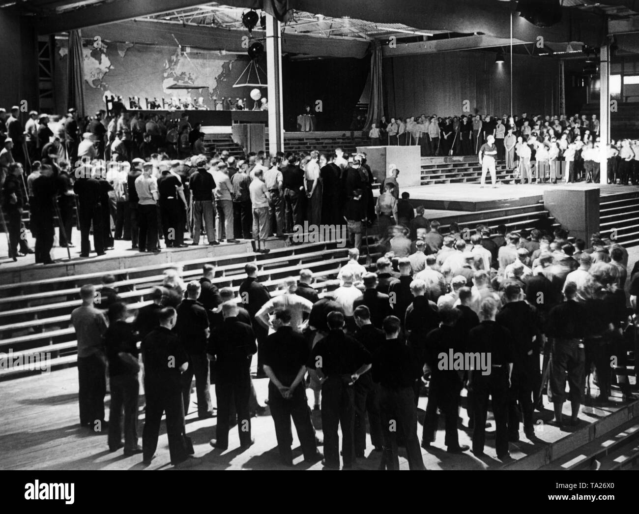 On the occasion of the first meeting of the Nazi organization 'Kraft durch Freude' ('Strength through Joy'), the theatrical performance 'Deutsche Heimkehr' ('German Homecoming') by Wilm Geyer is being performed in the Hanseatenhalle in Hamburg under the direction of Hellmuth Hansen and the participation of 2000 persons and 30 leading actors. Here, an excerpt from the 5th scene: In the background the conference of moneymakers with the symbolic scales in front of a world map. In the foreground the unemployed. Stock Photo