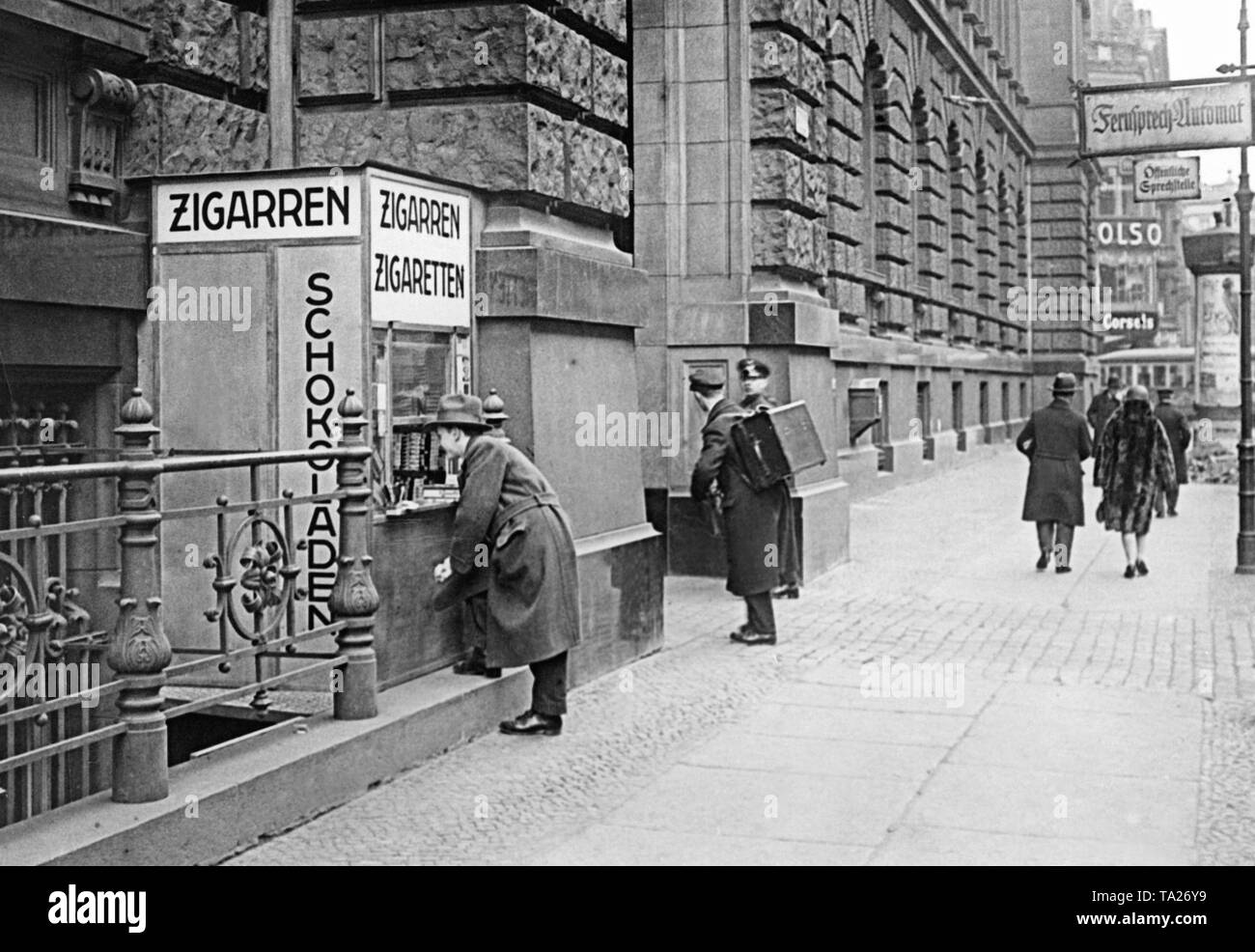 A kiosk advertises the sale of cigarettes and chocolate in the Mauerstasse in Berlin at the wall of a post office building. It is a modern stand made entirely of metal, and it is positioned so that it does not constrict the sidewalk and does not obstruct pedestrian traffic. Stock Photo