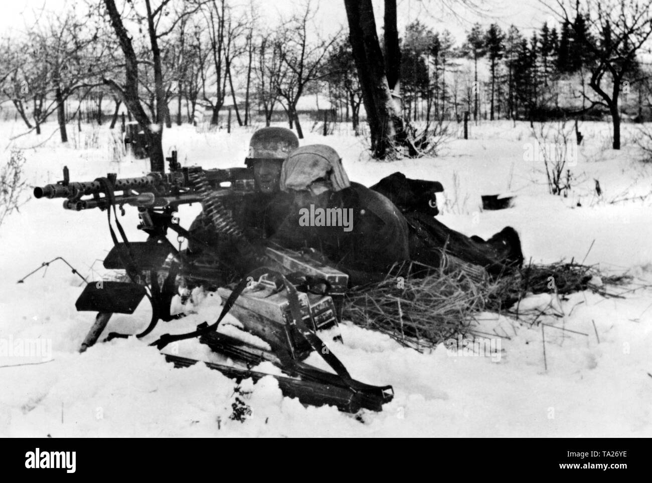On the edge of a small village west of Moscow, a German machine gun post with an MG 34 took position on a gun carriage. The soldiers try to protect themselves with some straw against the cold coming from below. (PK photo: war correspondent Schambortzky). Stock Photo