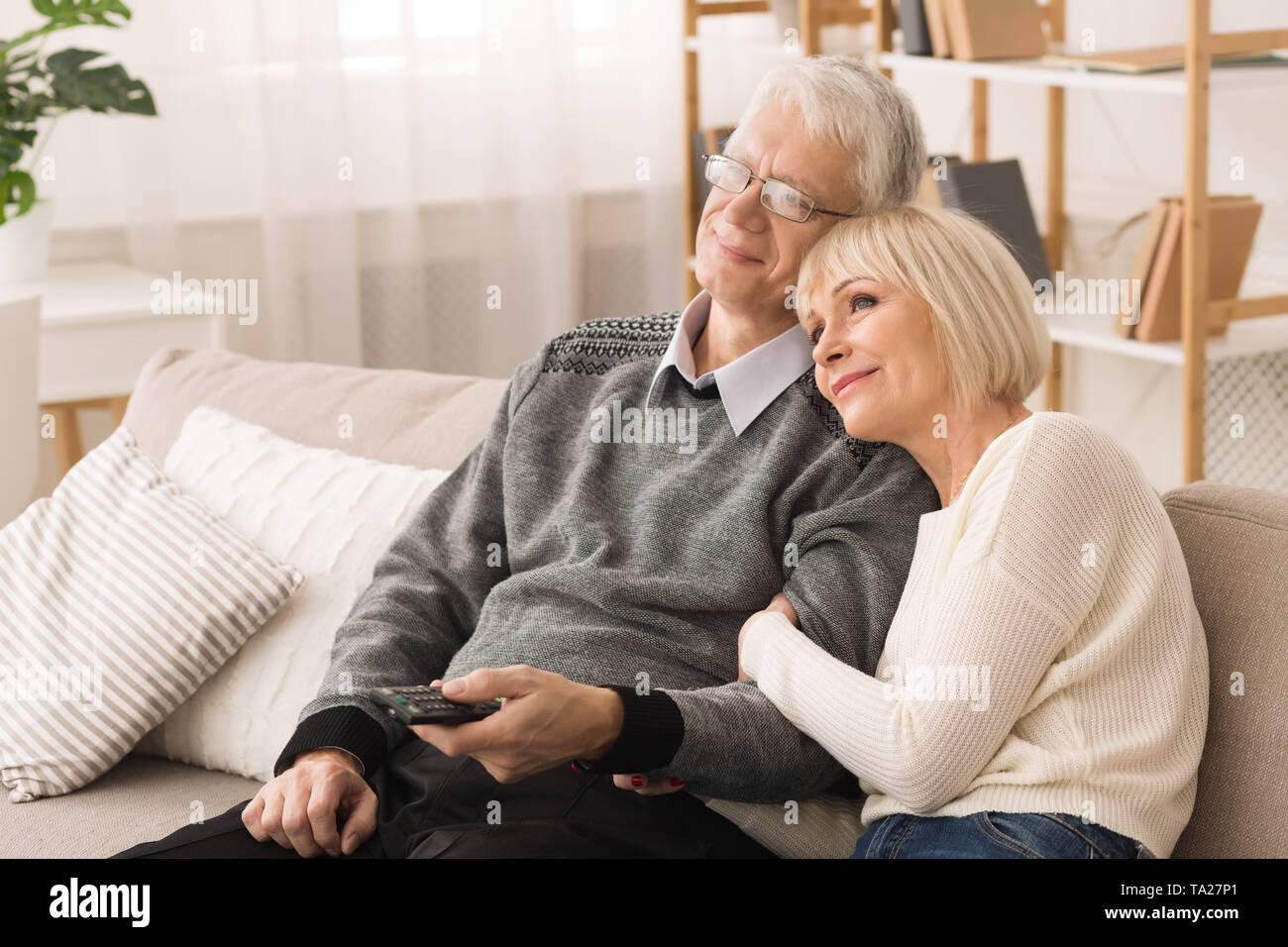 Loving Elderly Couple Watching TV, Resting At Home Stock Photo