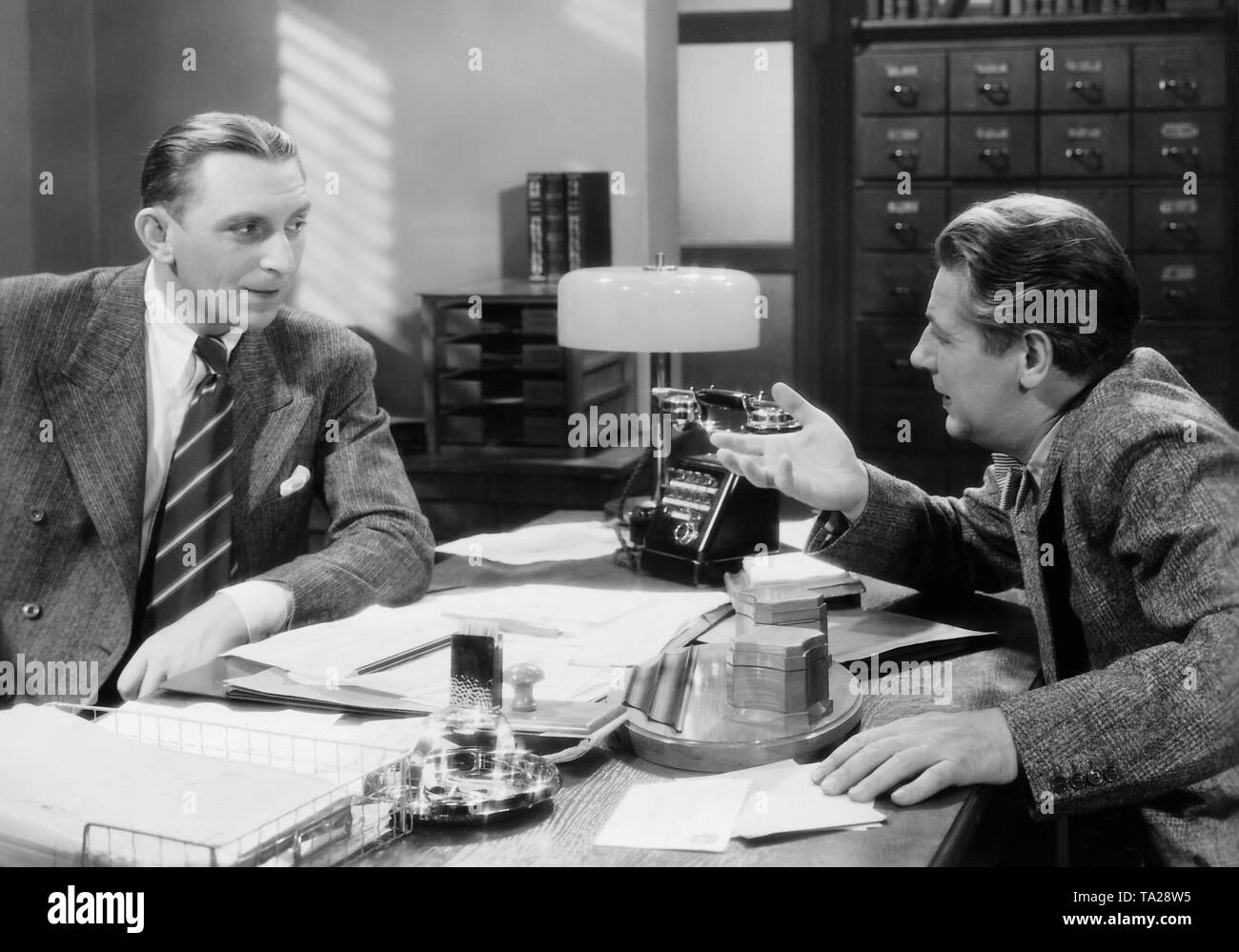 Theo Lingen (left) and Paul Hoerbiger (right) sit face to face at a desk in a scene in 'I Marry my Wife'. Stock Photo