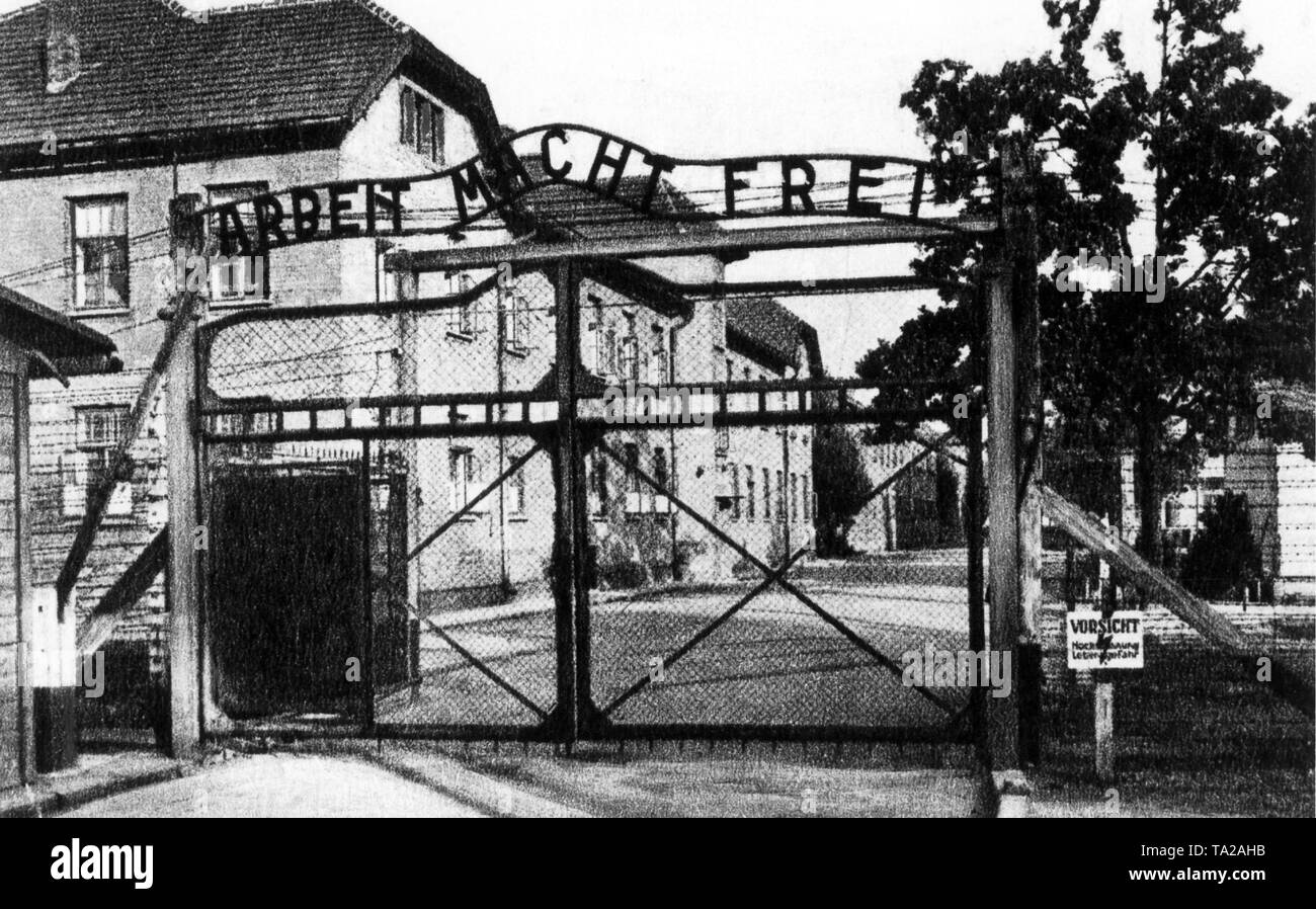 The main entrance to the Auschwitz-Birkenau concentration camp with the slogan 'Arbeit Macht Frei' (Work makes you free). The small sign saying 'Caution, high voltage, danger to life' refers to the outer barrier line secured with electric barbed wire. Stock Photo