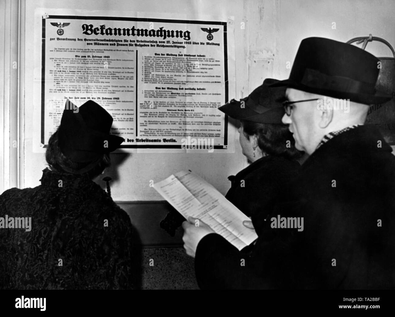 In the offices of Arbeitsamt Berlin hangs a notice on the Arbeitseinsatz (labour deployment). A man and two women are reading it through. Photo: Schwan Stock Photo