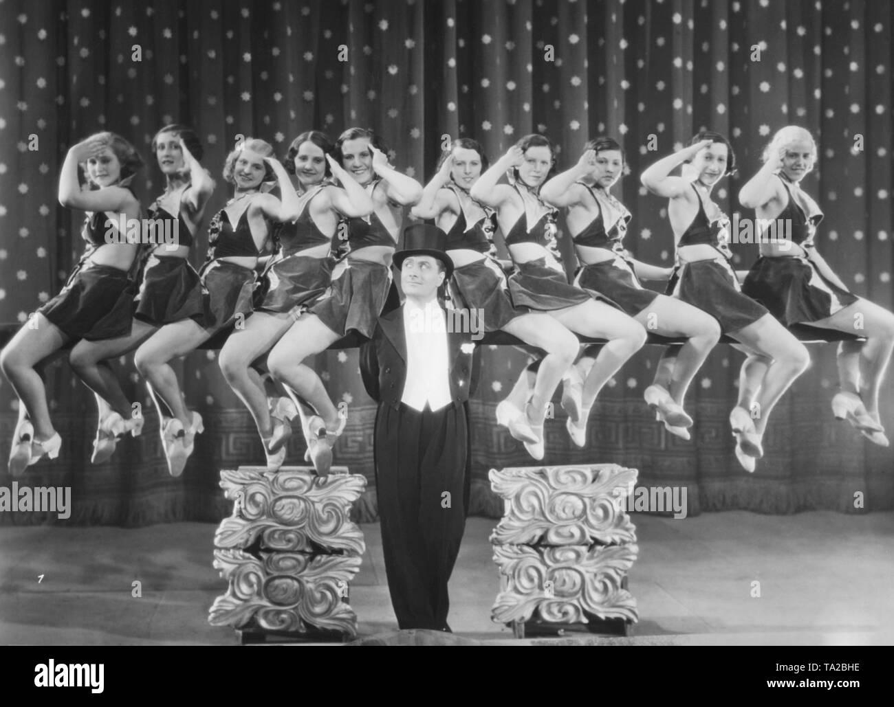 Scene from the movie 'Karneval der Liebe', directed by Paul Martin. In the foreground, the actor Hermann Thimig, who is depicted with five girls on each arm. The revue film is similar to the musical, the operetta and the dance film. The term refers to German and Austrian dance and music films. Features of the revue film are the light entertainment and the recurring dance and musical numbers, mostly contemporary hits. In some cases the revue film is a filmed music theater. Stock Photo