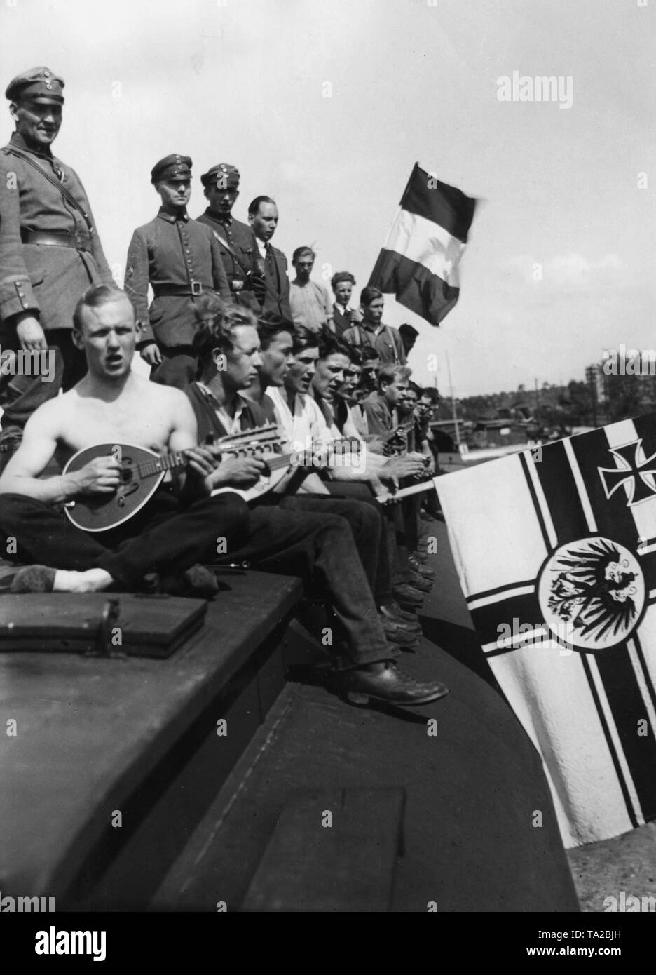 Workers of the volunteer work service of the Stahlhelm sing and play music on a personnel carrier of the Deutsche Reichsbahn (German National Railway), which is parked at the goods station Berlin-Koepenick as a sleeping car with kitchen. Beside the black-white-red imperial flag, the former imperial war flag of the German Empire. Stock Photo