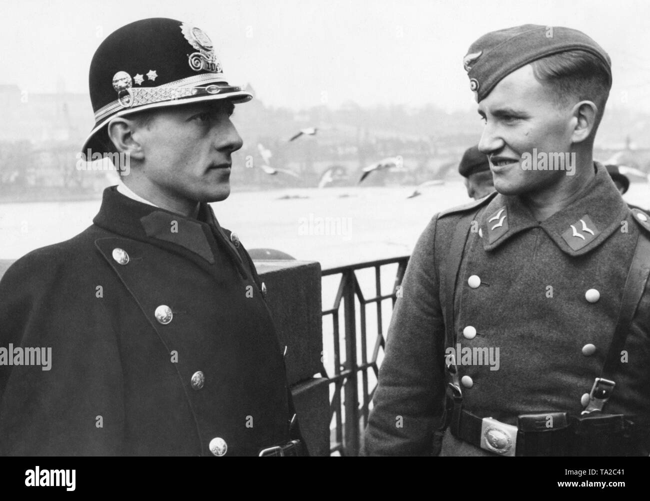 After the occupation of Bohemia and Moravia, the Protectorate of Bohemia and Moravia was established. A Czech policeman and a German soldier on a bridge in Prague. In the background, the Church of Mother of God before Tyn. Stock Photo