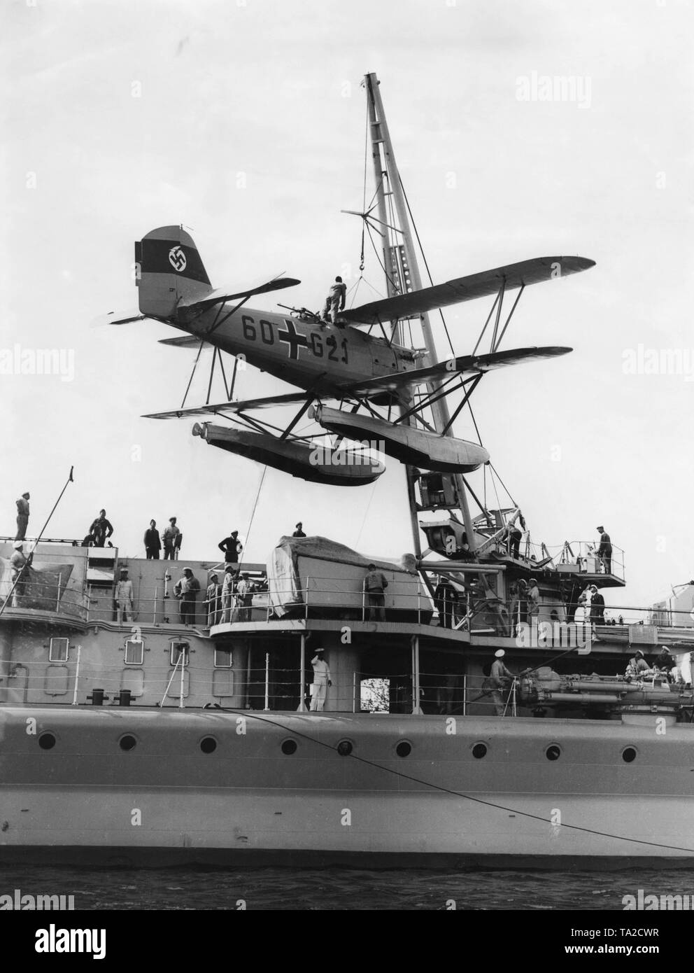 During a naval review at Swinemuende, the light cruiser 'Nuremberg' takes a watercraft on board with its crane. The aircraft is a Heinkel He 60. Stock Photo