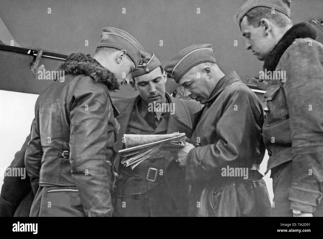 Photo of a briefing of fighter pilots with a commander (center, with a map) of a squadron of the Condor Legion under a wing of an airplane. Stock Photo