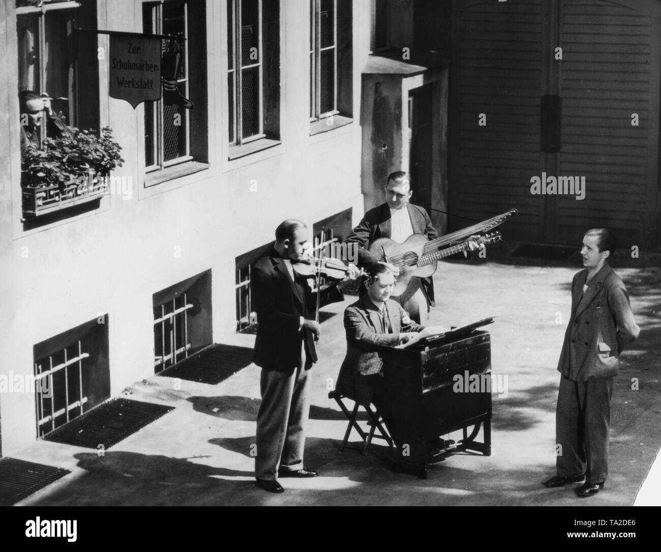 Four unemployed trying to make money as street musicians. A woman is looking at them from the window of a shoemaker's workshop. Presumably a moviestill. Stock Photo