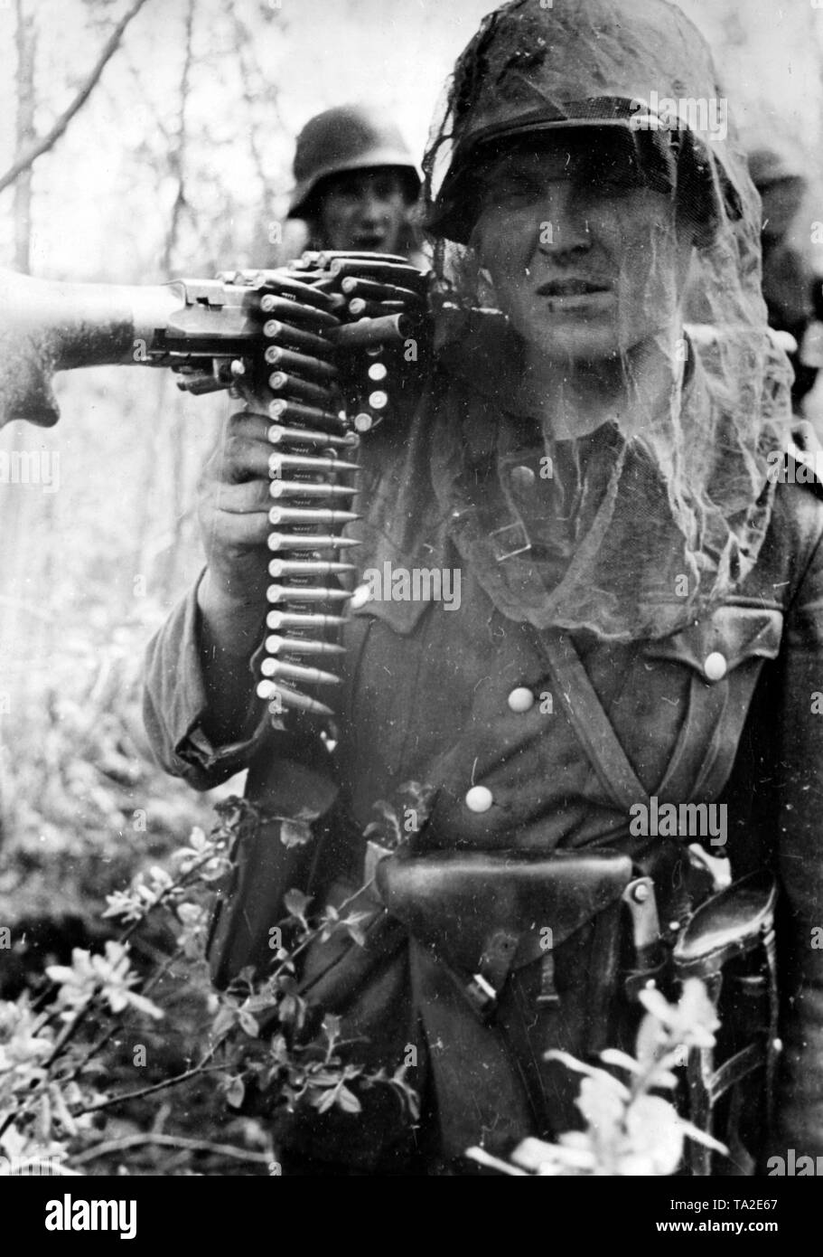 A German soldier with a mosquito net around his head carries a machine gun through the woods on the river Volkhov. Photo of the Propaganda Company (PK): war correspondent Ebert. Stock Photo