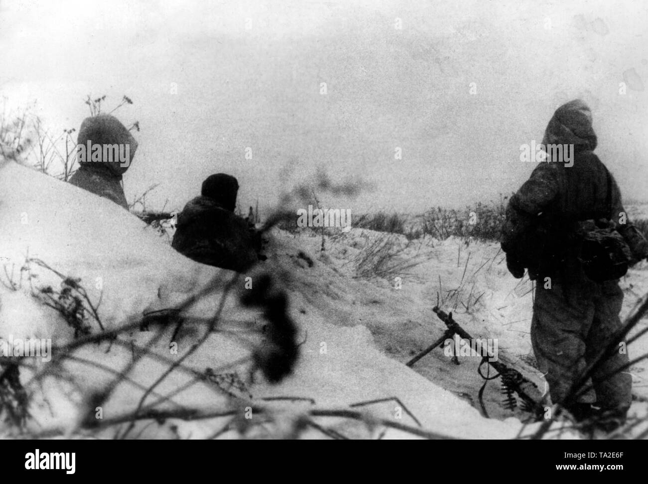 Three soldiers of an SS trooper unit at an unknown location on the Eastern Front. Armed with Maschinengewehr 34, they take shelter in a snow hollow. Photo of the Propaganda Company (PK): war correspondent Fritsch. Stock Photo