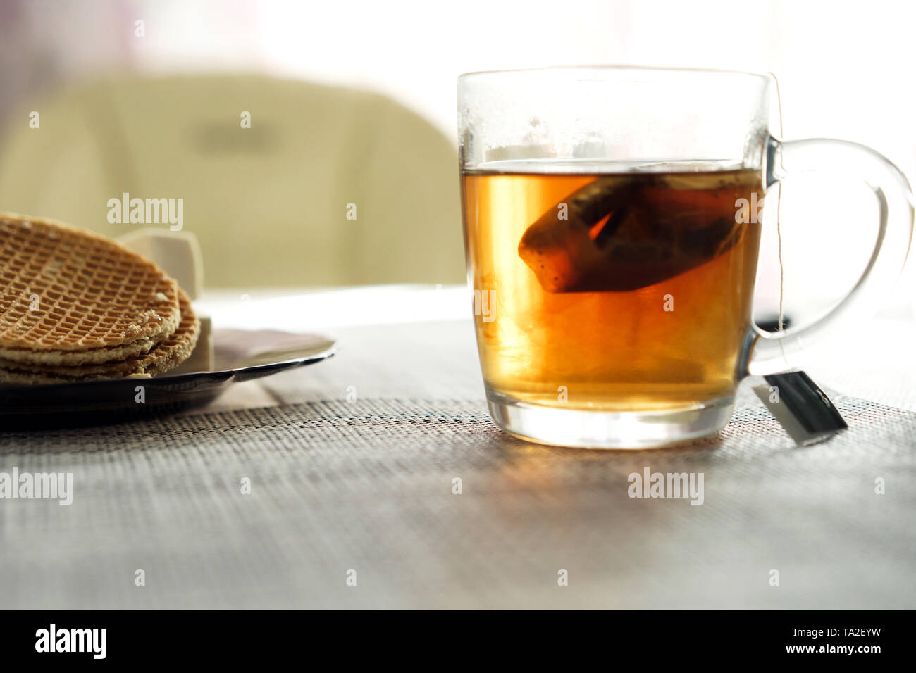 Transparent cup with brewed tea bag is on the table next to the plate Stock Photo