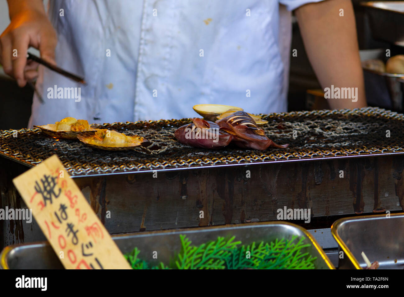 Man grilling squids and mushrooms at a food stall in Japan Stock Photo