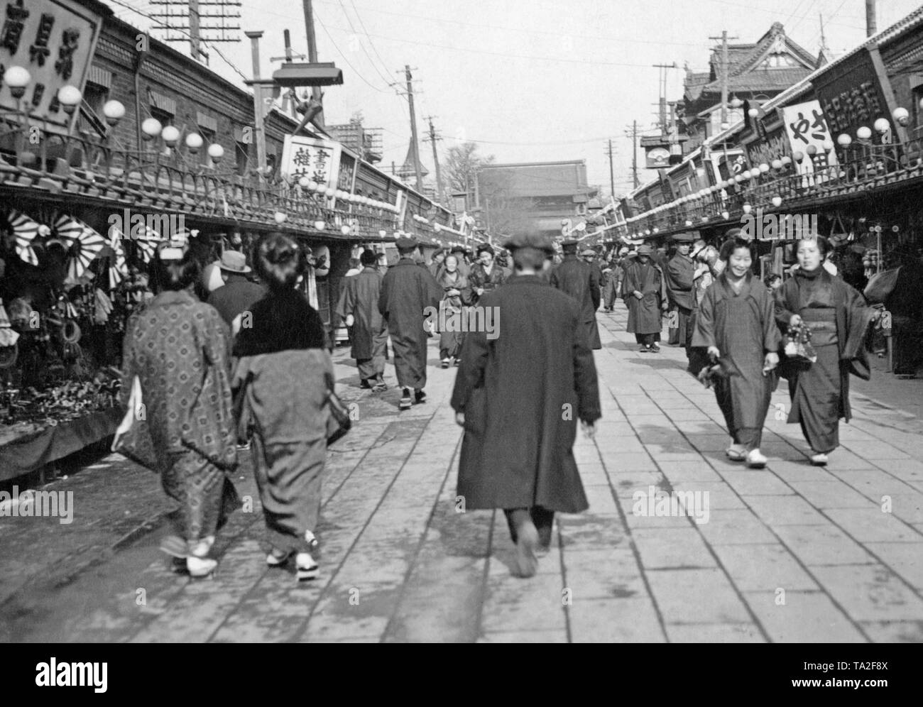 View along a street in Japan. On the left and right the street is lined with market stalls. Above it are attached lights and signs. (undated image, ca. 1930s) Stock Photo