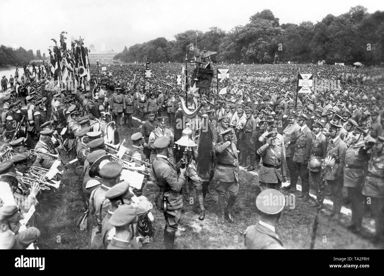 At the beginning of June, more than 100,000 members of the Stahlhelm gathered in Munich. The highlight of the event was the demonstration of the 100,000 members on the Isarwiesen and the march past of the Stahlhelm leaders Franz Seldte and Theodor Duesterberg. In the first row of the Gaue Potsdam, the Princes of Hohenzollern, Eitel Friedrich, August Wilhelm, and Oskar of Prussia. On the left a marching band is playing while Seldte and Duesterberg pass by and salute. Stock Photo