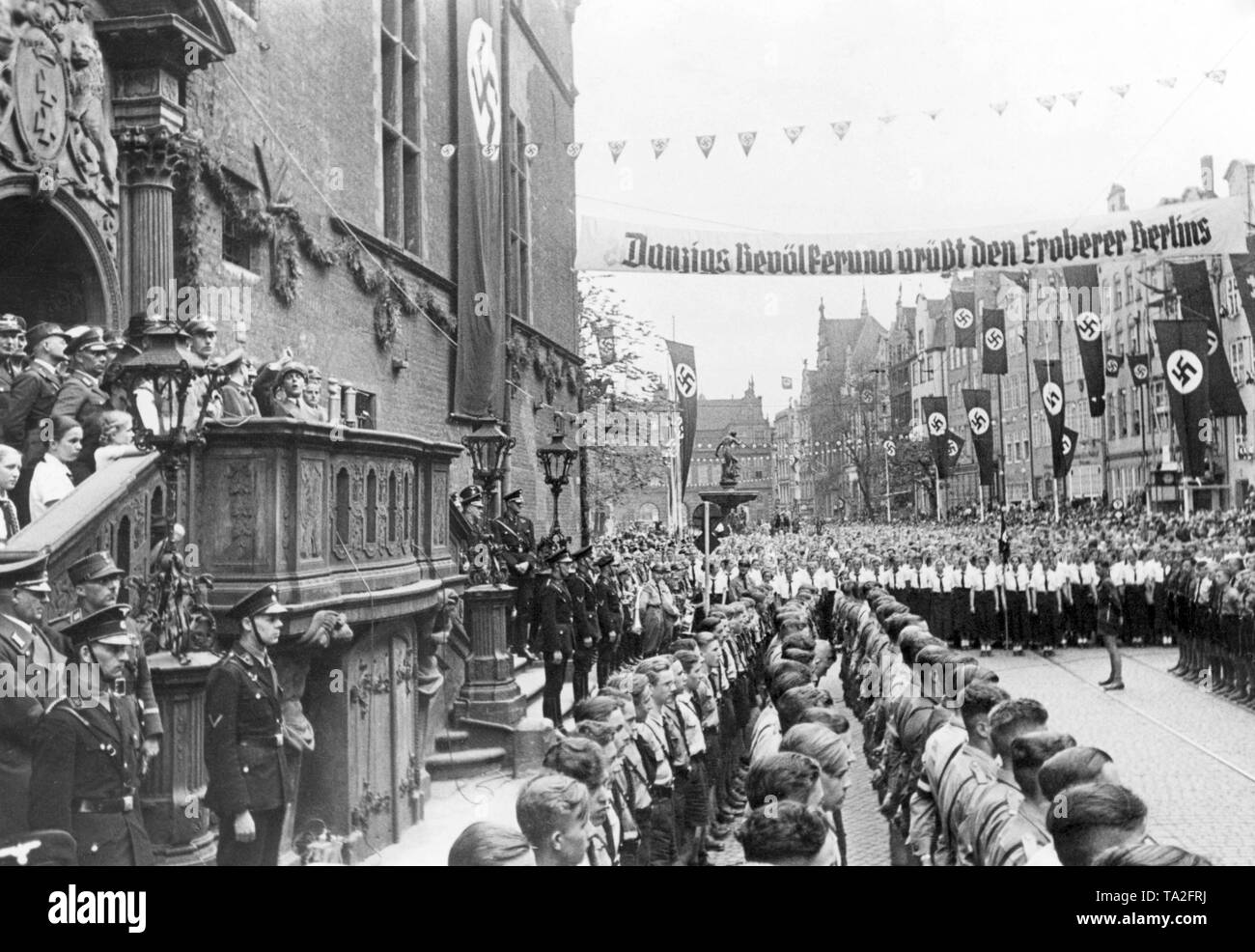 During his visit to Gdansk, the Minister of Propaganda, Joseph Goebbels, addresses to members of the Gdansk Youth Hitler Youth and BDM in front of the Town Hall of Gdansk. Across the street is a banner reading: 'Danzig's population greets the conqueror of Berlin.' The stairs of the Town Hall are guarded by SS and SA members. Stock Photo