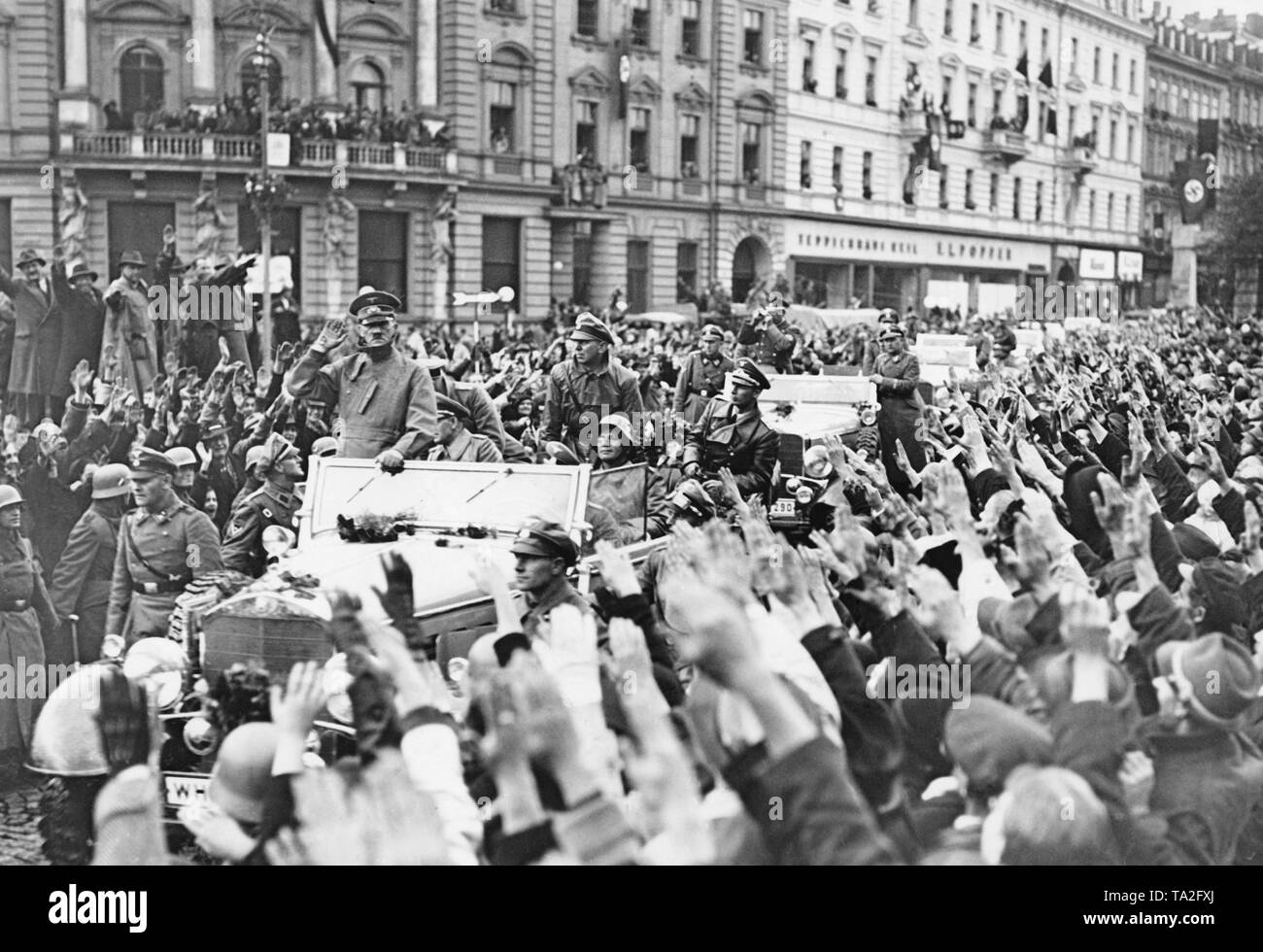 Adolf Hitler entering Karlsbad (today Karlovy Vary) on October 4, 1938. His motorcade is received cheerfully by the population. They are greeting him the Nazi salute. In his car in the back on the right, Adjutant of the Luftwaffe Nicolaus von Below. Sitting in front of him, General Walter von Reichenau. The bodyguards of the SS follow with other cars. Stock Photo