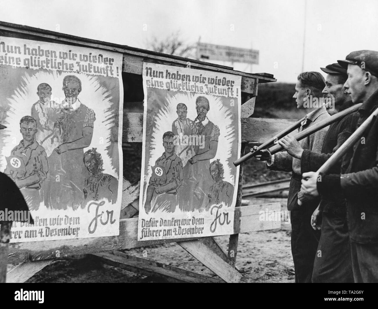 Men are observing an election poster for the Sudeten German by-elections in Dux (today Duchkov). In the plebiscite, votes are cast concerning the annexation of the Sudetenland to the German Reich. On the poster, a family and the inscription: 'Now we have a happy future again! We thank the Fuehrer with a yes on December 4'. Stock Photo