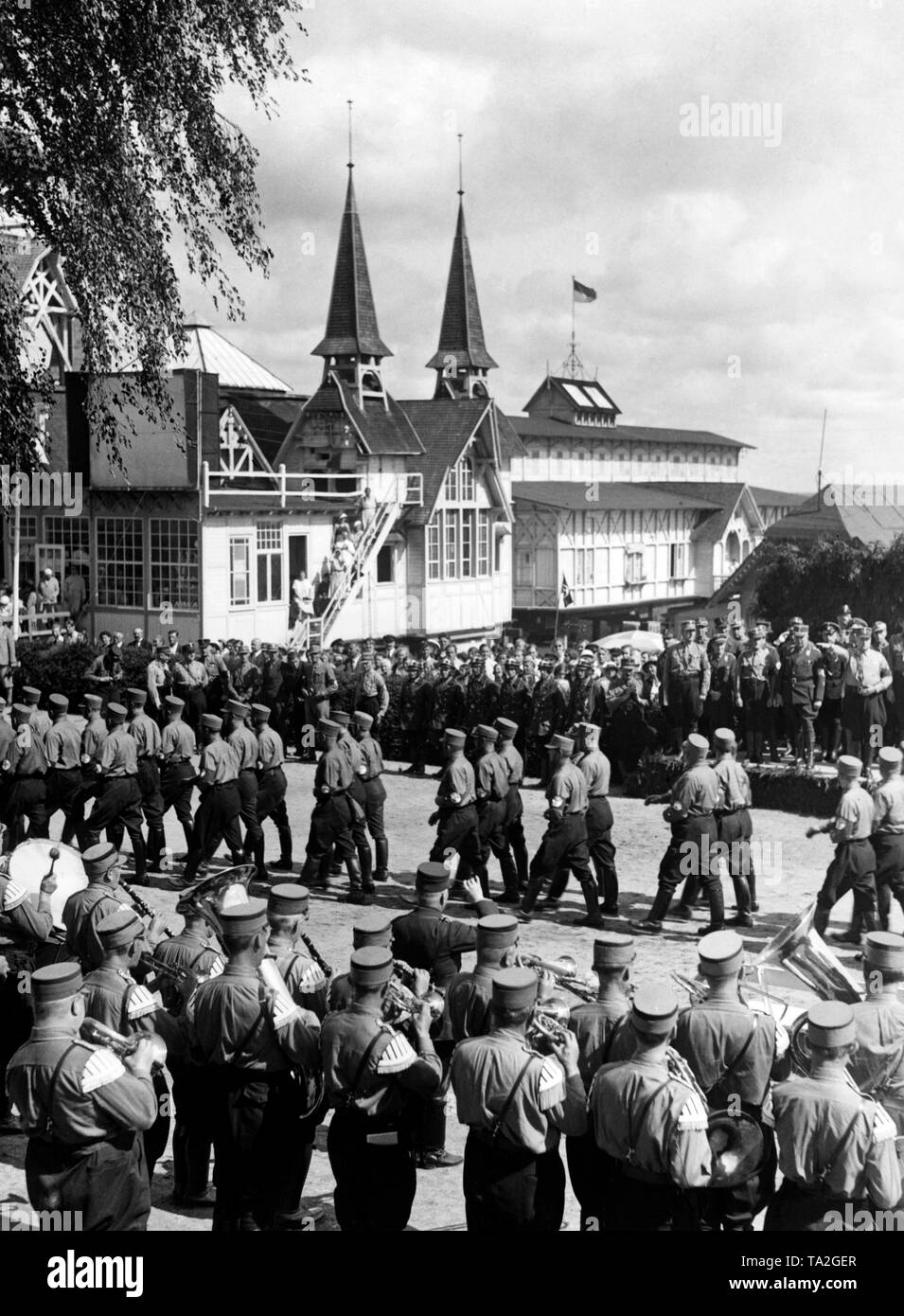 Delegations of the Nationalsozialistisches Kraftfahrerkorps (National Socialist Motor Corps) are marching after their sports tour to Heringsdorf on Usedom past Oberfuehrer (senior leader) Herbert Schnull. In the foreground, a brass band. Stock Photo
