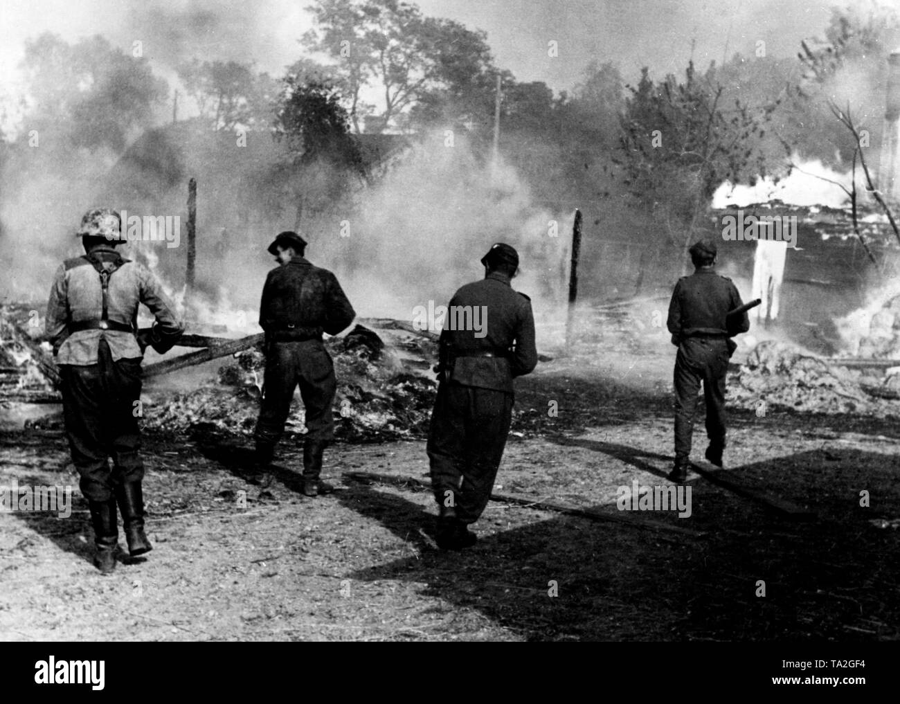 German soldiers search a burning village with drawn weapons on the Eastern Front (presumably Eastern Poland). The houses that were mostly built of wood caught fire by heavy Soviet artillery fire. Photo of the Propaganda Company (PK): war correspondent Koenneke. Stock Photo