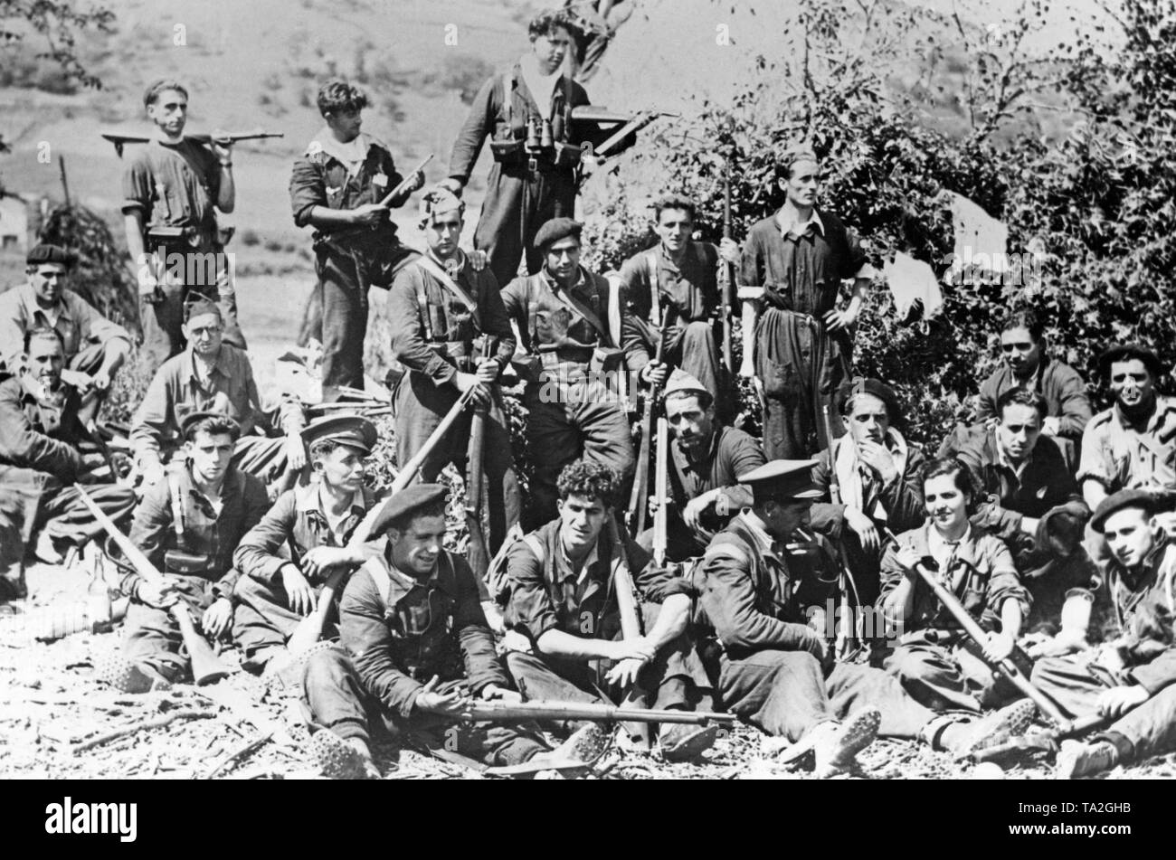 Group photo of Republican fighters of the People's Front during the battle of San Sebastian (Donostia) on the Northern Front in the Basque Country. The soldiers wear uniforms or blue overalls and are armed with rifles. They are wearing nailed boots. On the right, a woman. In the background, hills. Stock Photo