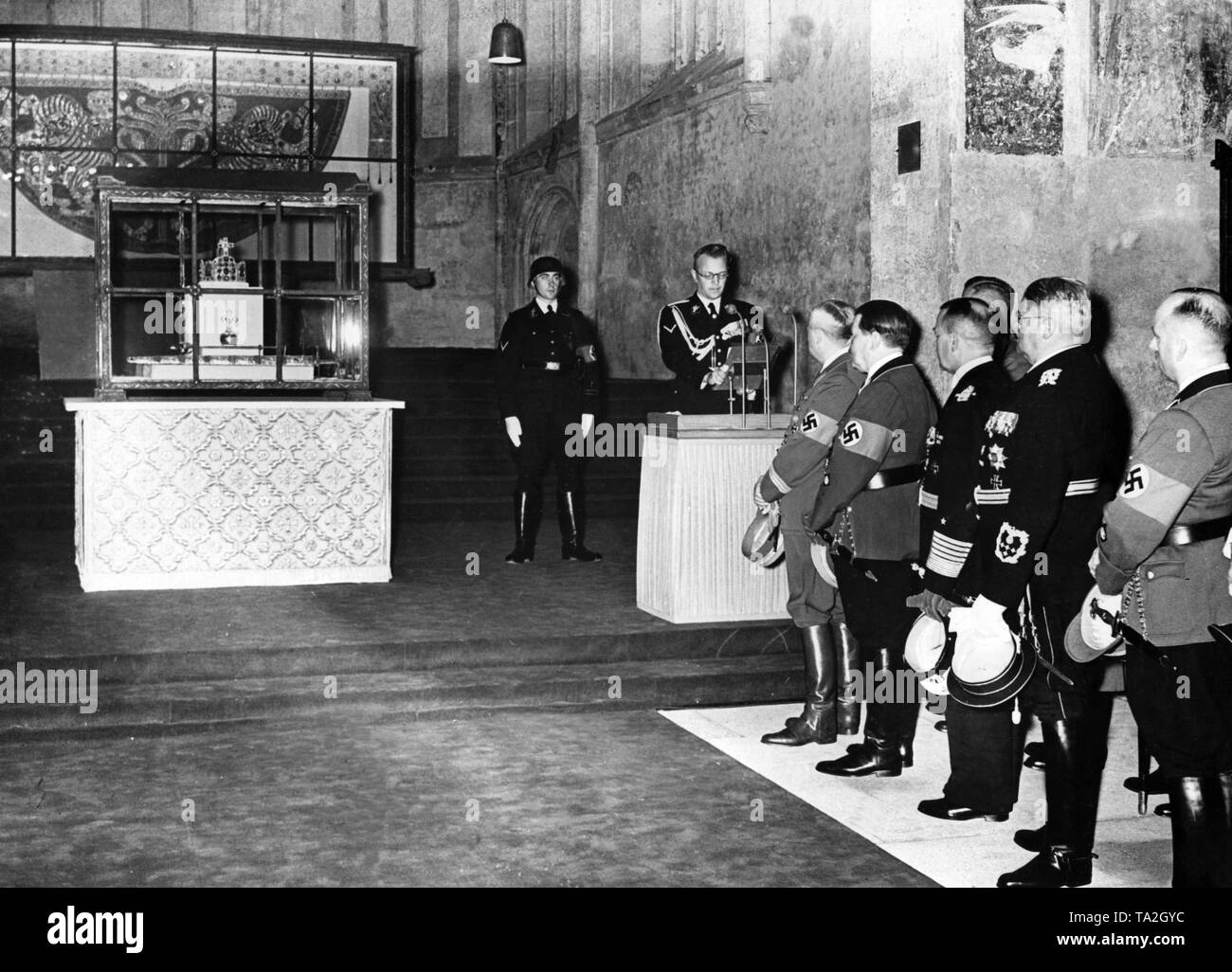 The Imperial Regalia (Reichskleinodien) is handed over to the mayor of Nuremberg, Mayor Willy Liebel, by the Austrian Reich Governor Arthur Seyss-Inquart (at the lectern) in the Katharinenkirche (St. Catherine's Church) in Nuremberg, where they are also on exhibition. Before Seyss-Inquart, listening to him (from left): Hanns Kerrl, Wilhelm Ohnesorge, Generaladmiral Erich Raeder, State Minister Dr. Otto Meissner. To the left of Seyss-Inquart, a guard of the SS. Stock Photo