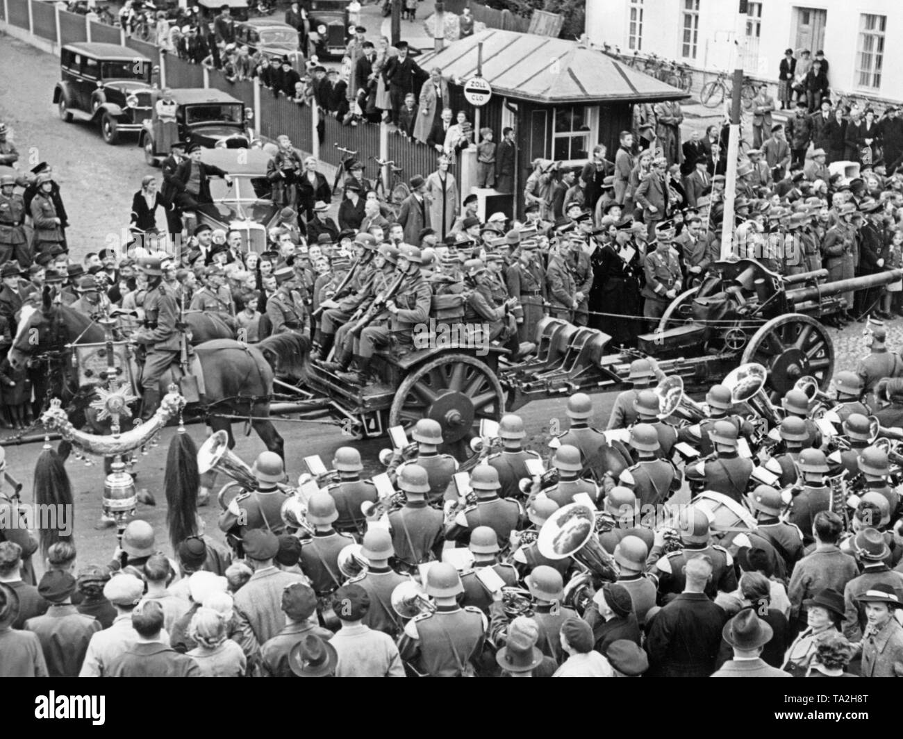 German troops (10.5 cm leFH 18 light howitzer) cross the former German-Czechoslovak border at Ebersbach / Georgswalde (today Jirikov) on October 2, 1938. People greet the soldiers with the Nazi salute. In the foreground, a brass band. Stock Photo