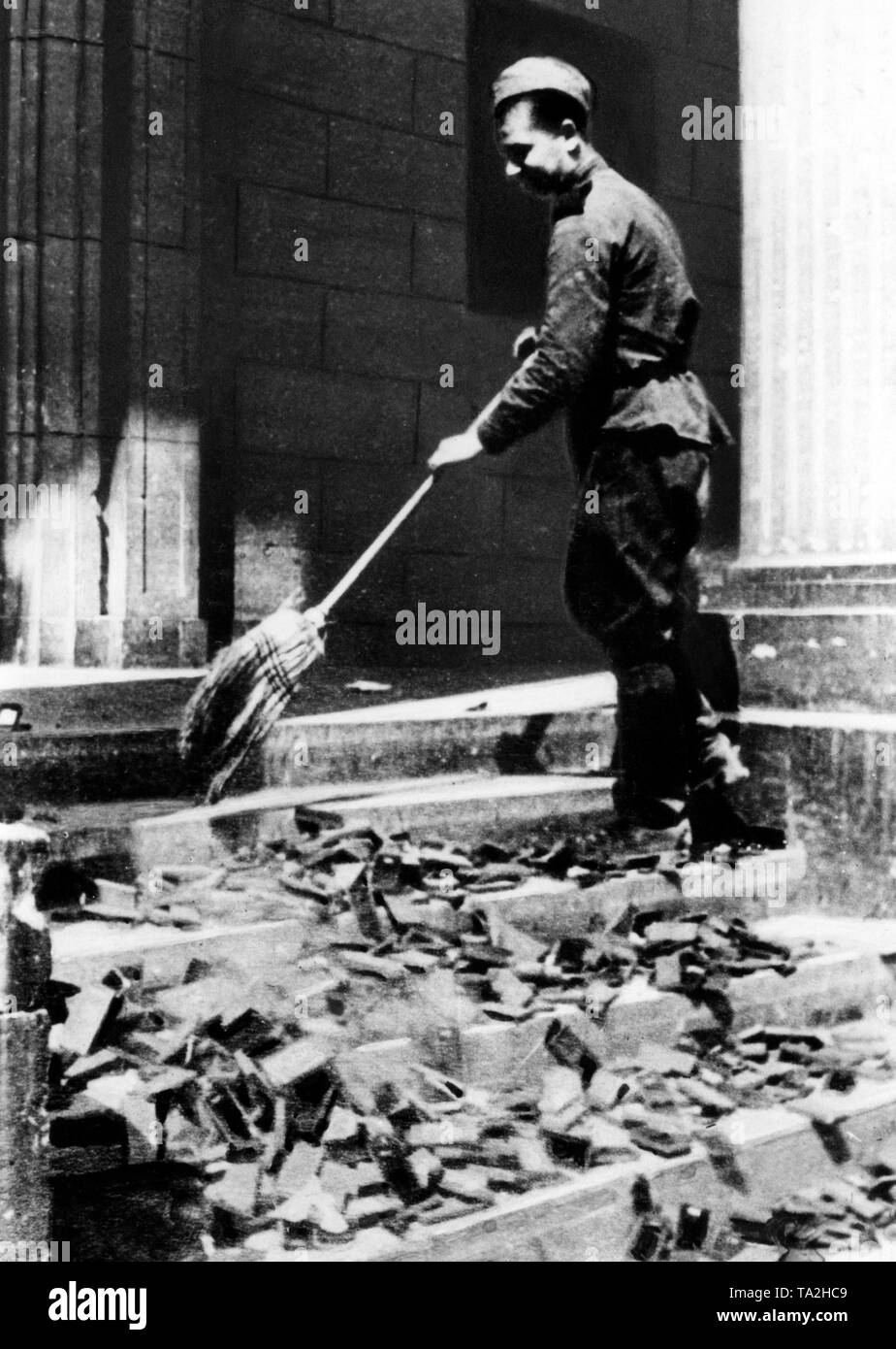A few days after the end of the Battle of Berlin, a Soviet soldier sweeps  German war decorations and medal boxes down the steps of the ruined Reichstag building. Stock Photo