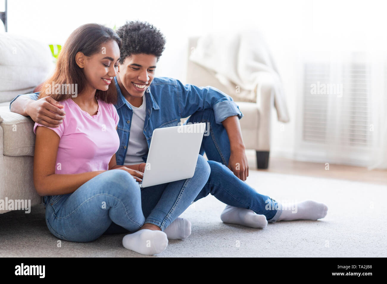 Black boy and girl using laptop, sitting on floor together Stock Photo