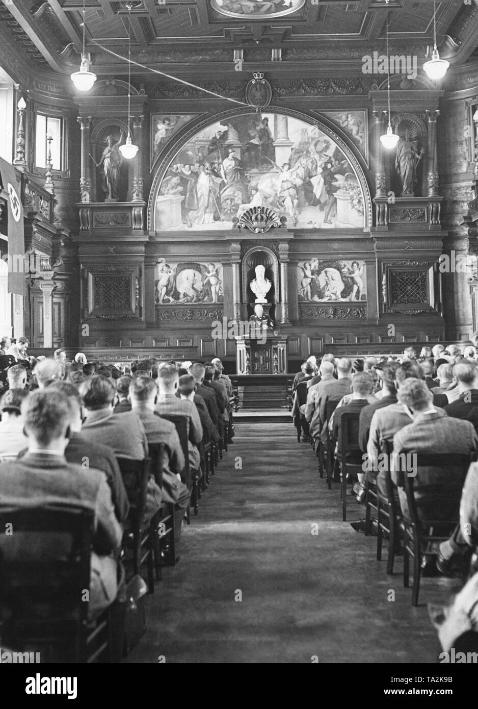 Dr. Paul Schmitthenner, Minister of State and Head of the Ministry of Culture, dressed in SS uniform, gives a lecture in the auditorium filled with listeners in the building of the Old Heidelberg University. A swastika flag is hanging on the wall. The photo was taken on the occasion of the 550th anniversary of the Heidelberg University. Stock Photo