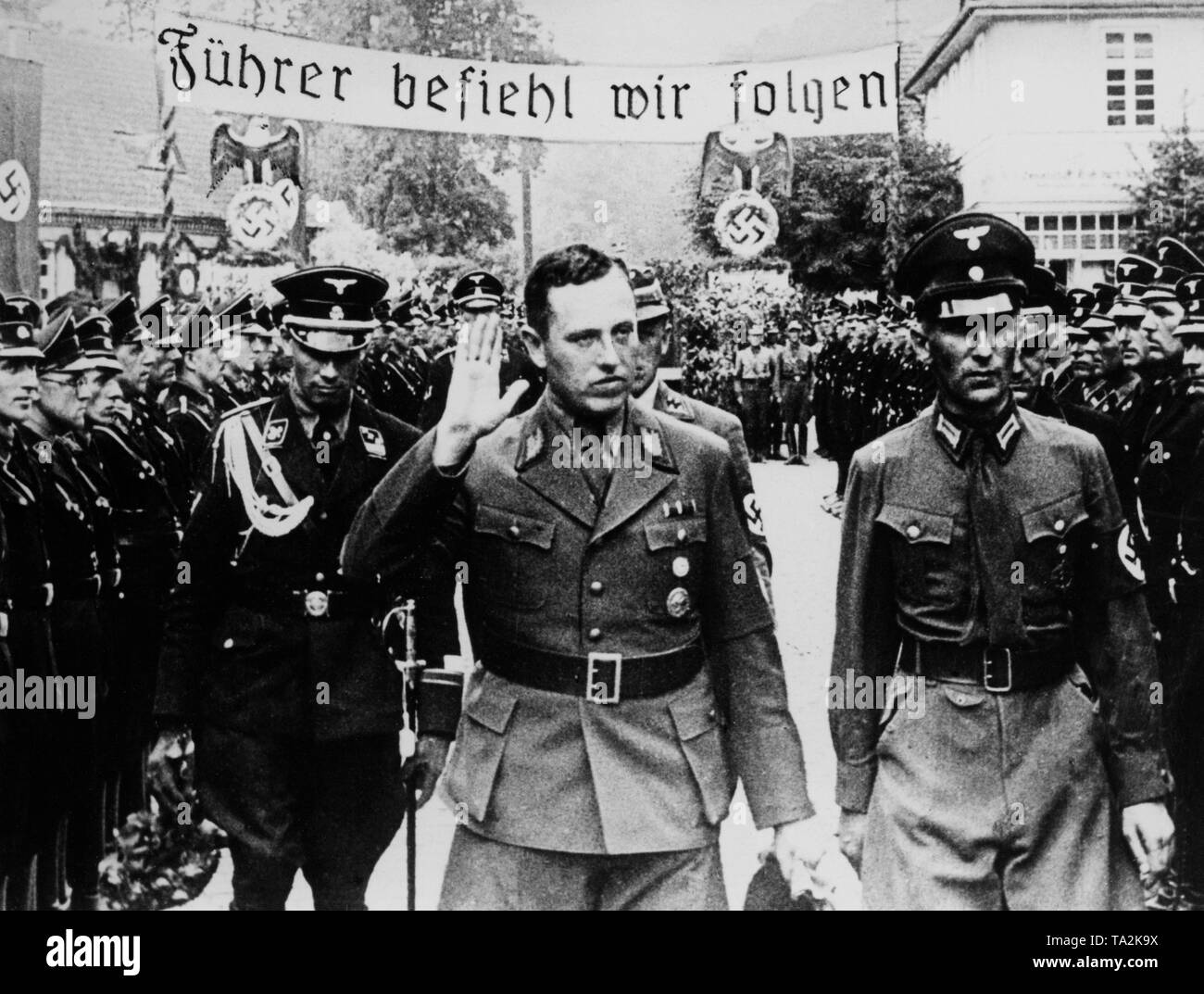 Albert Forster, the Nazi Gauleiter of Gdansk, (middle) takes the salute of members of the SS-Heimwehr Gdansk, SS-Wachsturmbann Eimann during a meeting of the District Leader of the NSDAP in the Free City of Gdansk. On a banner stands the slogan: 'Fuehrer befiehl-wir folgen!' ('The Fuehrer commands, we follow'), behind it the Nazi sovereignty symbols of the German Reich. Stock Photo