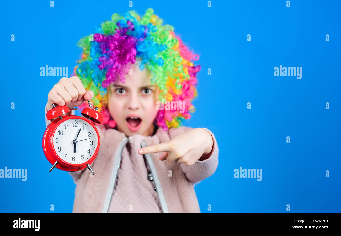 The clock ticking away the time. Adorable small child with colorful wig