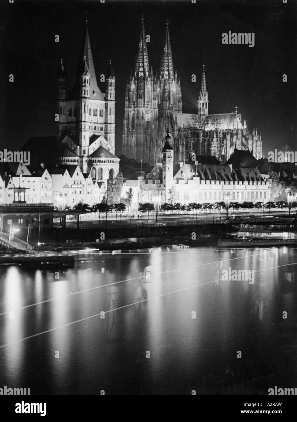 View of the Cologne Rhein Shore. On the promenade the Great St. Martin Church (left) and the Stapelhaus (right next to it). In the background, the Cologne Cathedral. The buildings are illuminated with spotlights. Stock Photo