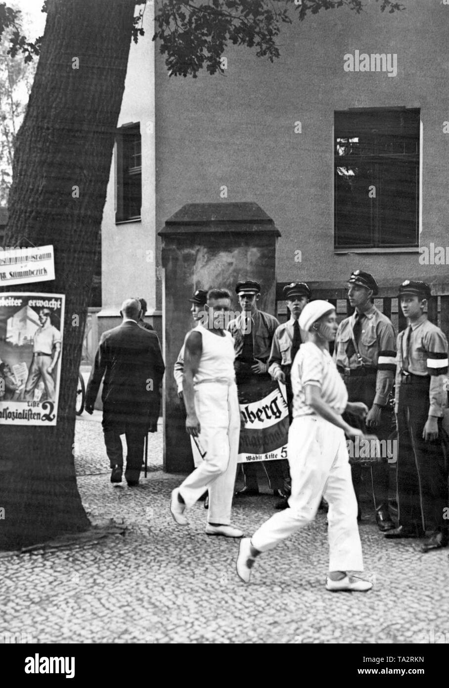 Water sportsmen on their way to the polling station in Mirbachstrasse in Potsdam on the occasion of the Reichstag election. On a tree, left in the foreground there is an election poster of the NSDAP with the call 'Workers wake up'. On the right in the background there are the supporters of the Kampffront Schwarz-Weiss-Rot with an election poster of the German National People's Party, which campaigns for Hugenberg. Stock Photo