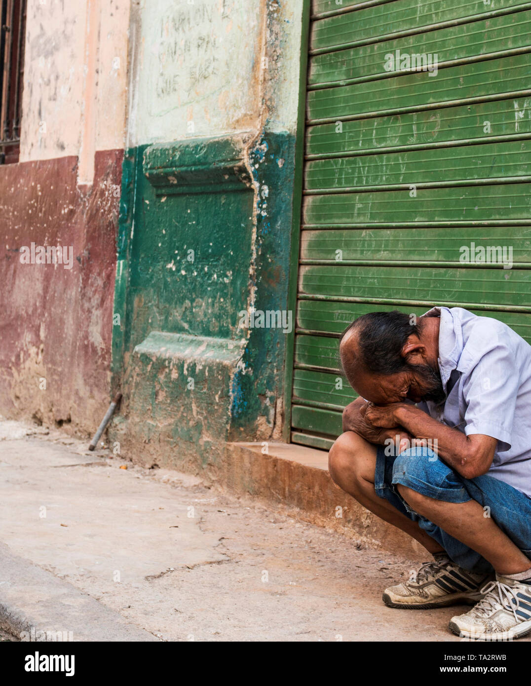Havana, Cuba - 25 July 2018: Cuban man looks to be in dispair sitting on a ledge in front of old run down building in Old Havana Cuba. Stock Photo