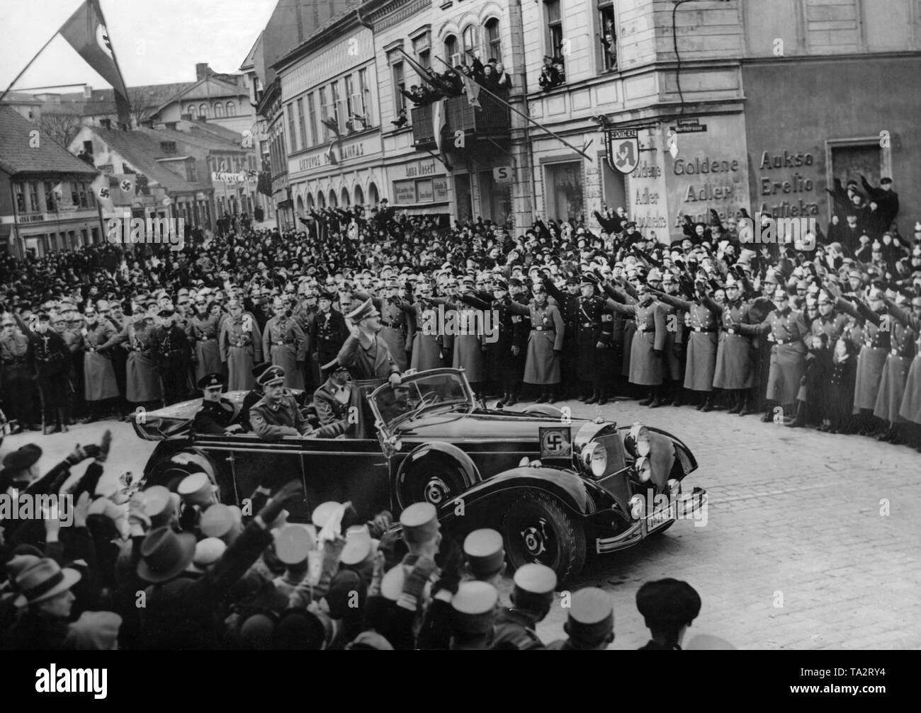 Adolf Hitler is driving triumphantly through the city of Memel (Klaipeda) in a Mercedes, here in the Werftstrasse, where he is cheered by the population for the incorporation of the Memelland into the German Reich. Behind in the car at left, Generaladmiral Erich Raeder. Stock Photo
