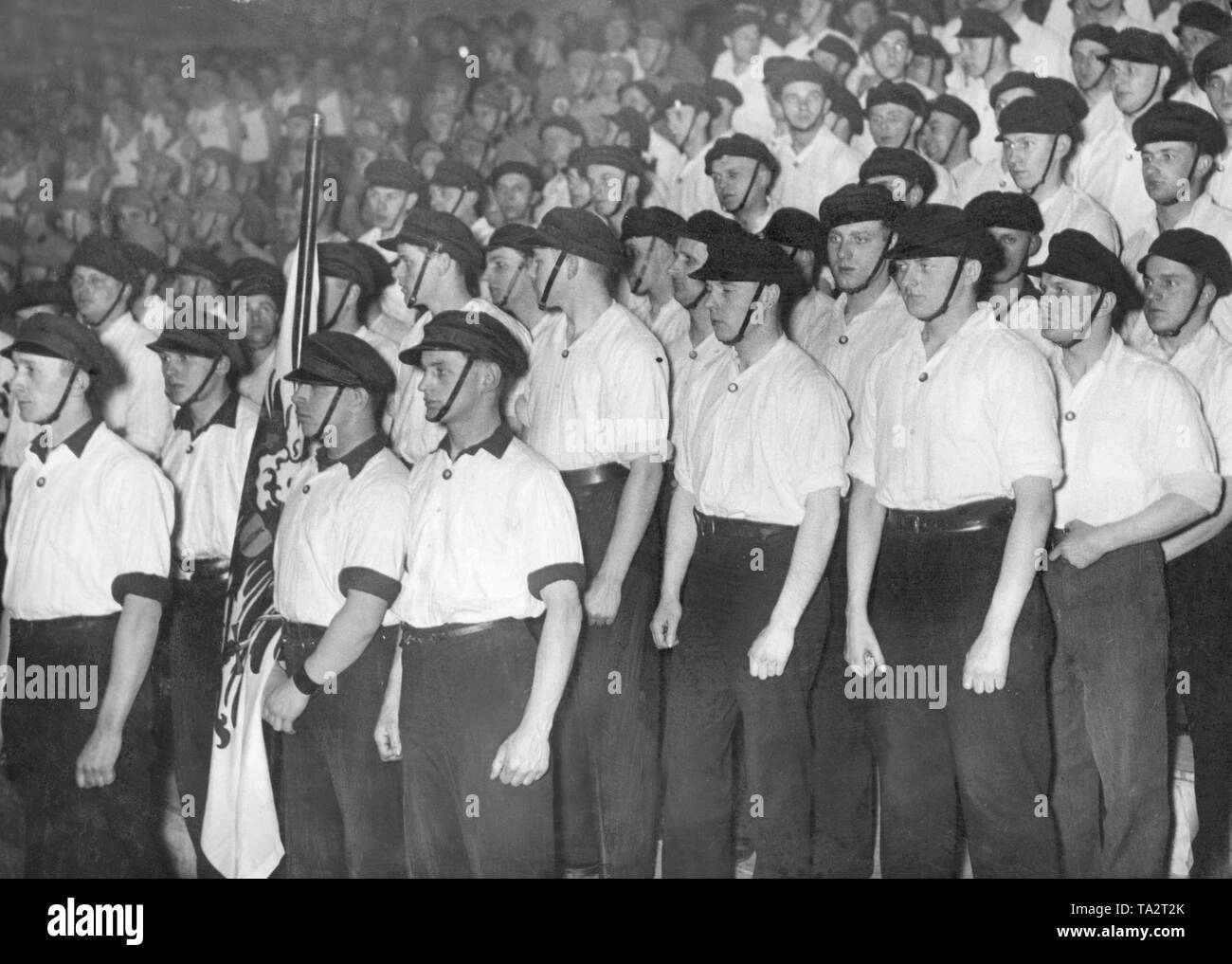 Members of an SA-Sturm have line up during a mass event of the NSDAP. They are wearing uniform white shirts and caps. Stock Photo
