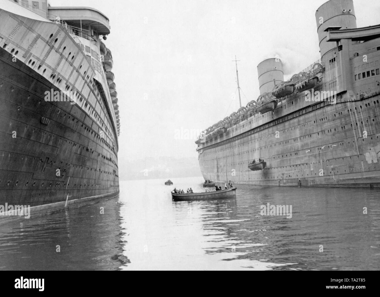 Crew members of the 'Queen Elizabeth' (r.) practice the release of lifeboats. On the left in the picture is the French ocean liner 'Normandie'. Stock Photo