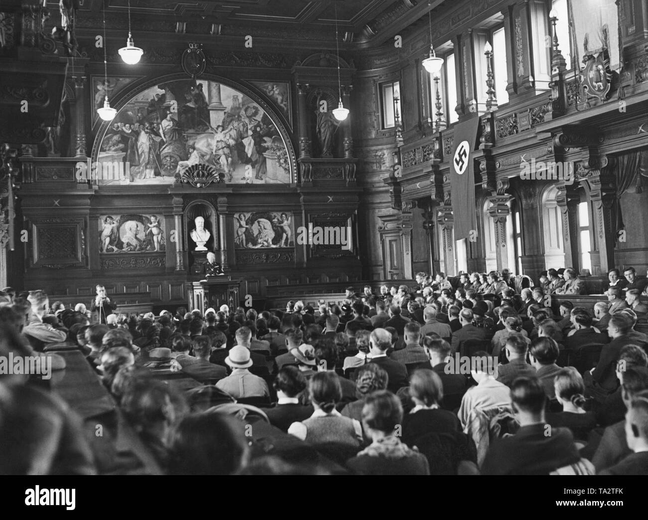 Dr. Paul Schmitthenner, Minister of State and Head of the Ministry of Culture, dressed in SS uniform, gives a lecture in the auditorium filled with listeners in the building of the Old Heidelberg University.A swastika flag is hanging on the wall.The photo was taken on the occasion of the 550th anniversary of the Heidelberg University. Stock Photo