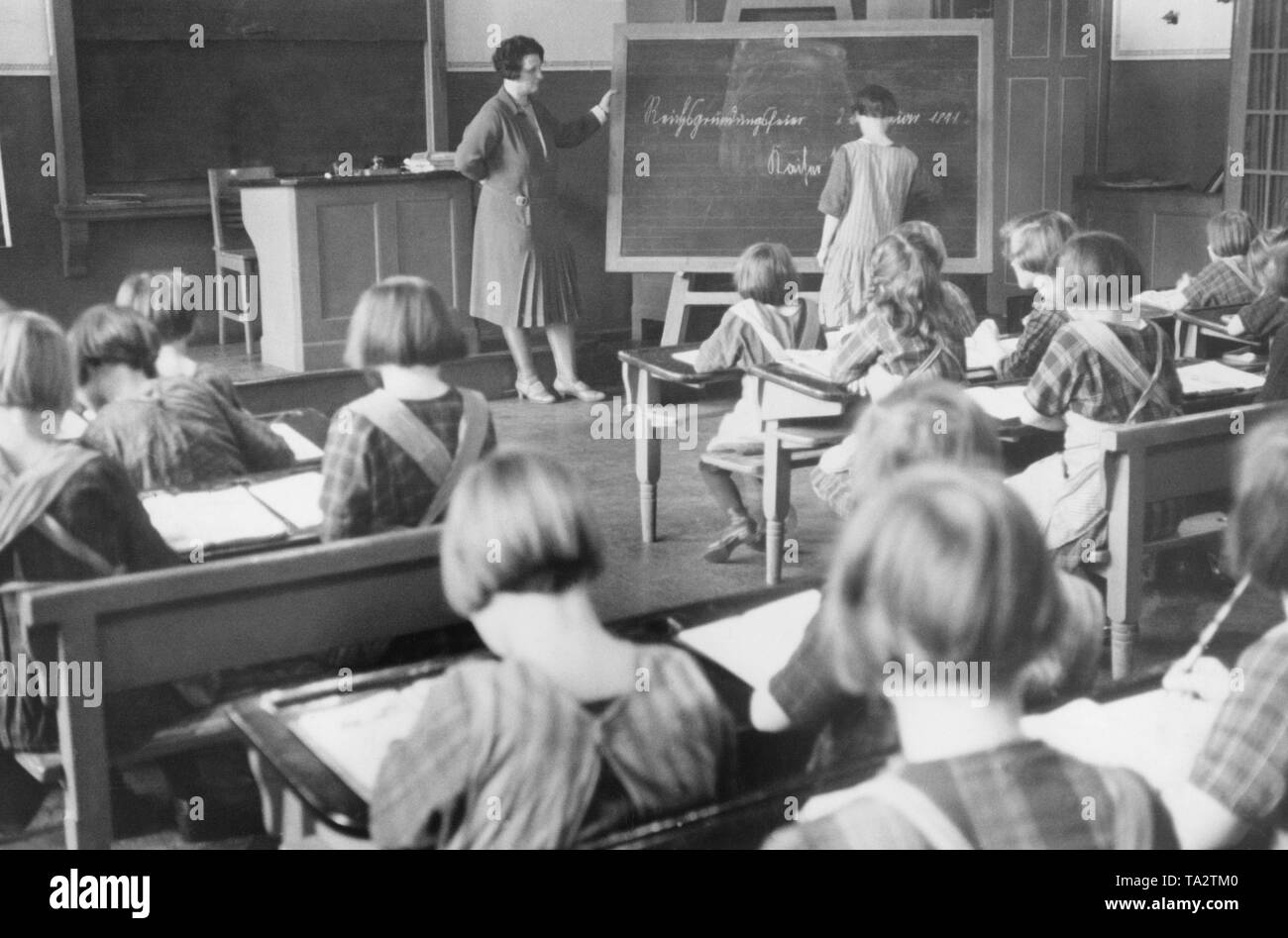 View into the classroom during a school lesson for girls in a Berlin orphanage, presumably in 1931. A schoolgirl stands in front and writes with chalk on the blackboard 'Kaiser Wilhelm I.', on the board is already written 'Reichsgruendungsfeier [...] 1871' (Foundation ceremony of the Reich). Stock Photo