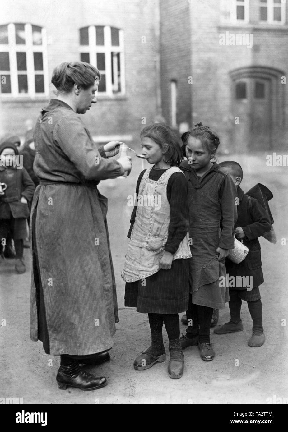 A woman gives cod liver oil to the children of a Berlin school. Four children are standing in a row in front of her. Stock Photo