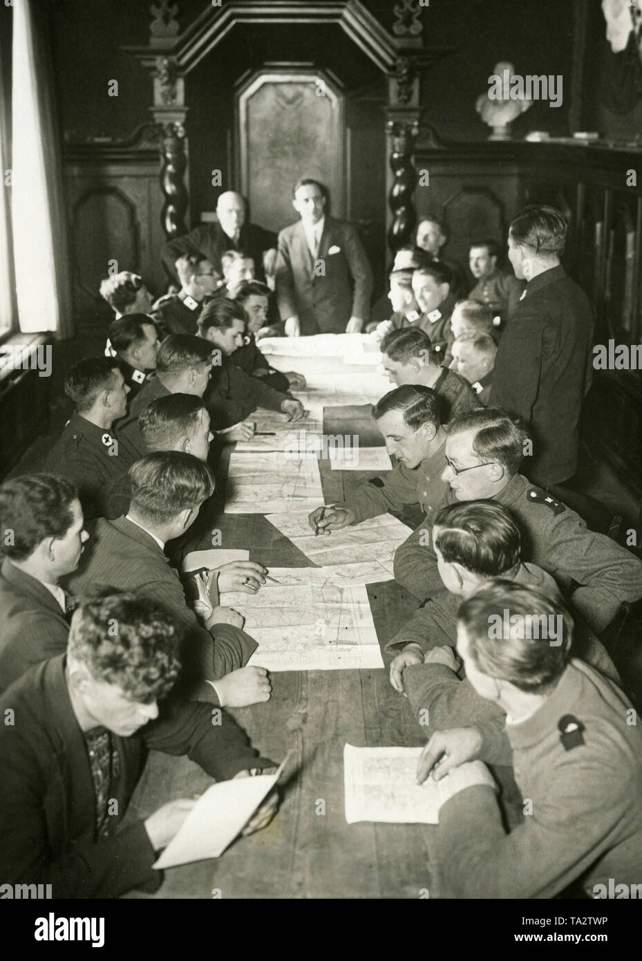 The Berlin Red Cross takes over the training of young unemployed people in its 'Notwerk deutscher Jugend' (Emergency Organization for German Youth). Young men, some in field uniform or the uniform of the Red Cross study maps of Doeberitz at a long table. Paramilitary sports was part of the training of the organization and Doeberitz, as a former military school offered enough space to accommodate the young people, so the photo was probably made there and shows the group shortly before a field exercise. Stock Photo