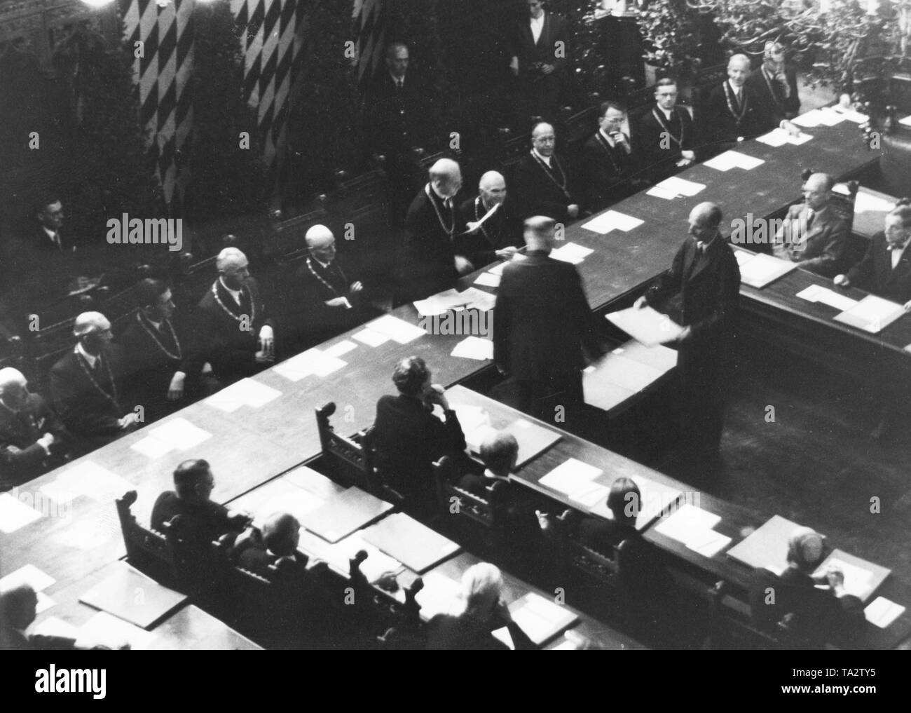 During the first council meeting in the small meeting room of the Munich Town Hall, the Lord Mayor Karl Scharnagl, who was appointed by the Allies, hands over letters of appointments to the 36 city councilmen. Stock Photo