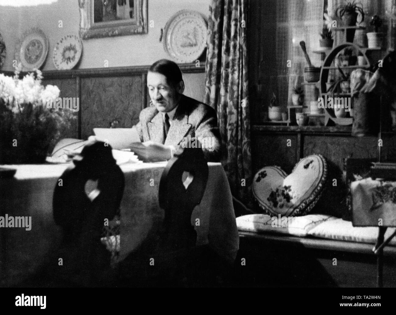 Adolf Hitler reads a letter in the dining room of his country house 'Wachenfeld' on Obersalzberg. Right on the bench is a pillow in the form of a heart. Stock Photo