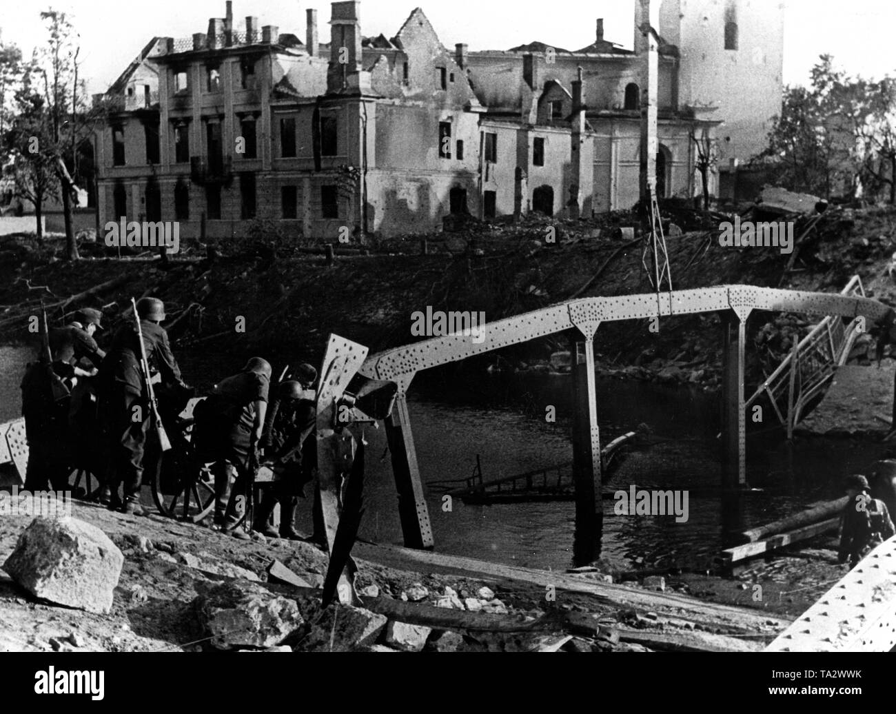 German soldiers try to carry a light infantry gun (presumably 7,5-cm-leichtes Infanteriegeschuetz 18) over a destroyed bridge in a Latvian village. Photo of the Propaganda Company (PK): war correspondent Weber. Stock Photo